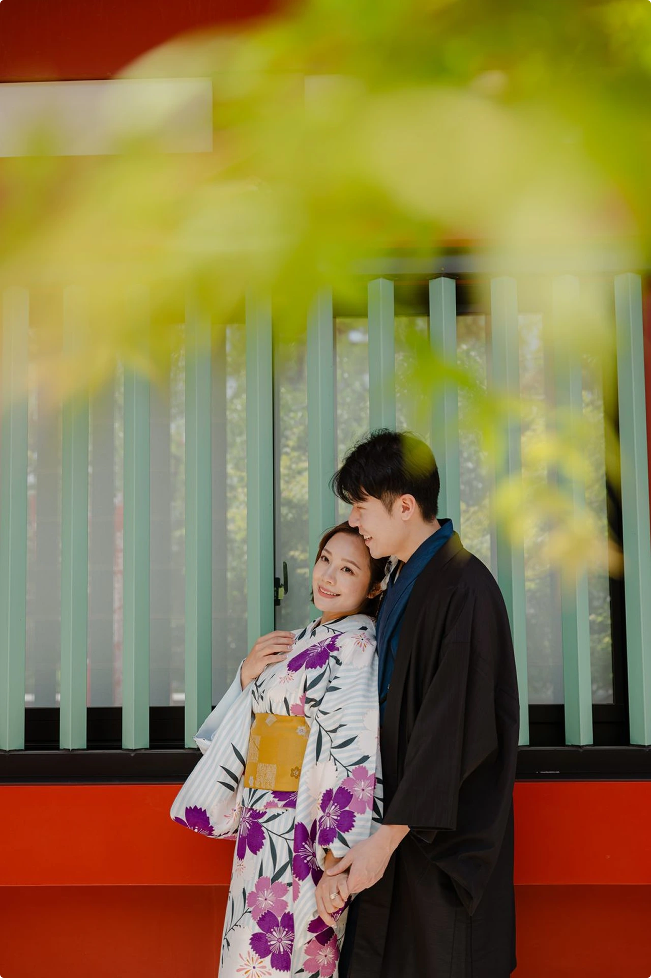 Couple in kimono embracing under maple leaves outside a vermilion shrine
